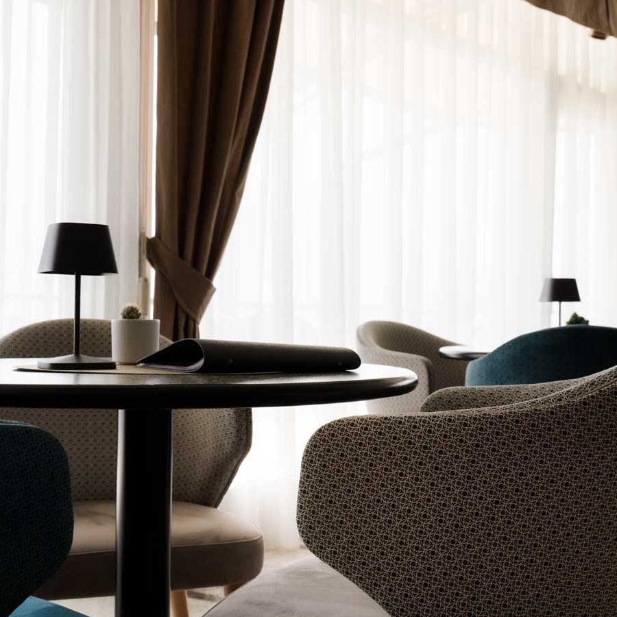 Sedie artigianali di design, rivestite con tessuti luminosi e forme eleganti, esposte nell’incantevole sala da pranzo dell’Hotel Astor